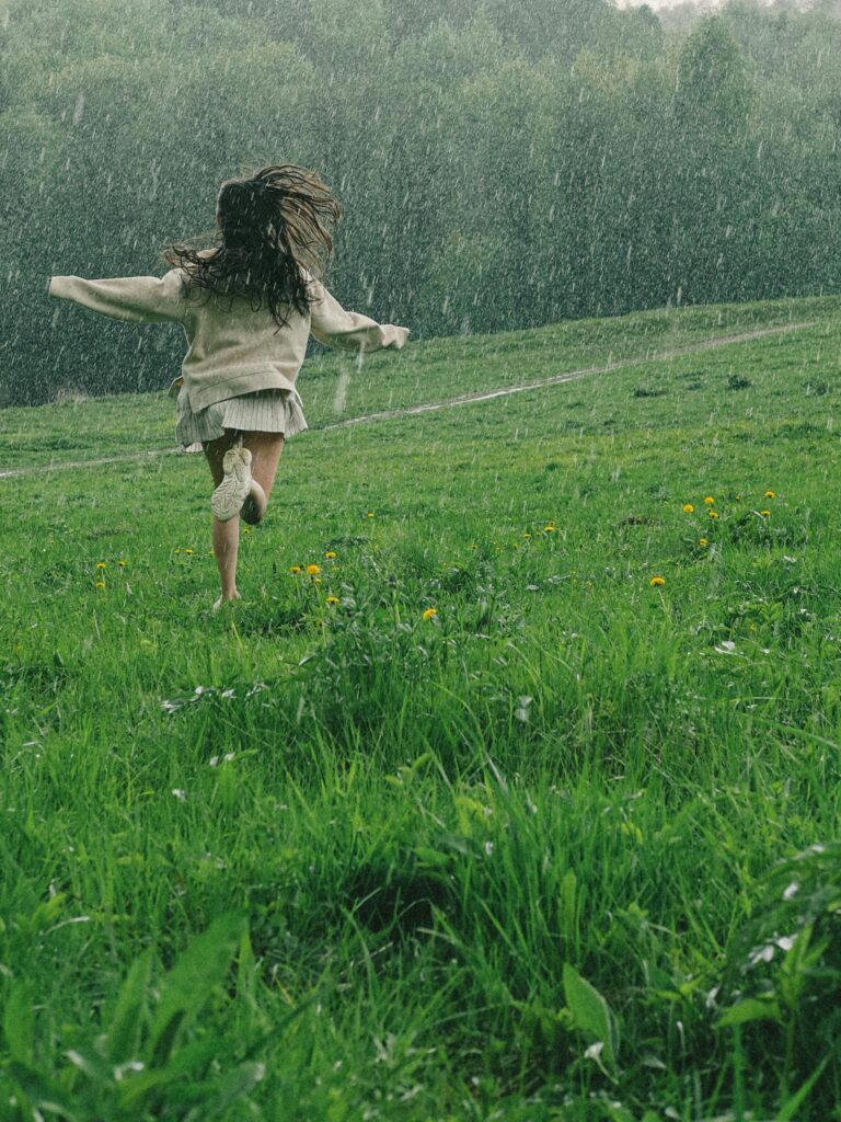 A person runs through a vibrant green field during a serene spring rain shower.